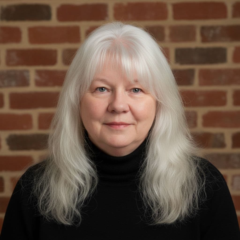 Donna Rougeau, smiling, with long silver hair and a black turtleneck, in front of a brick wall